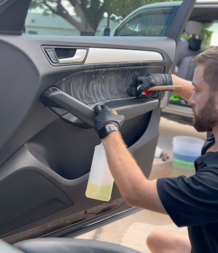Alex from Detail Daddy deep cleaning a car door panel with brushes and cleaner